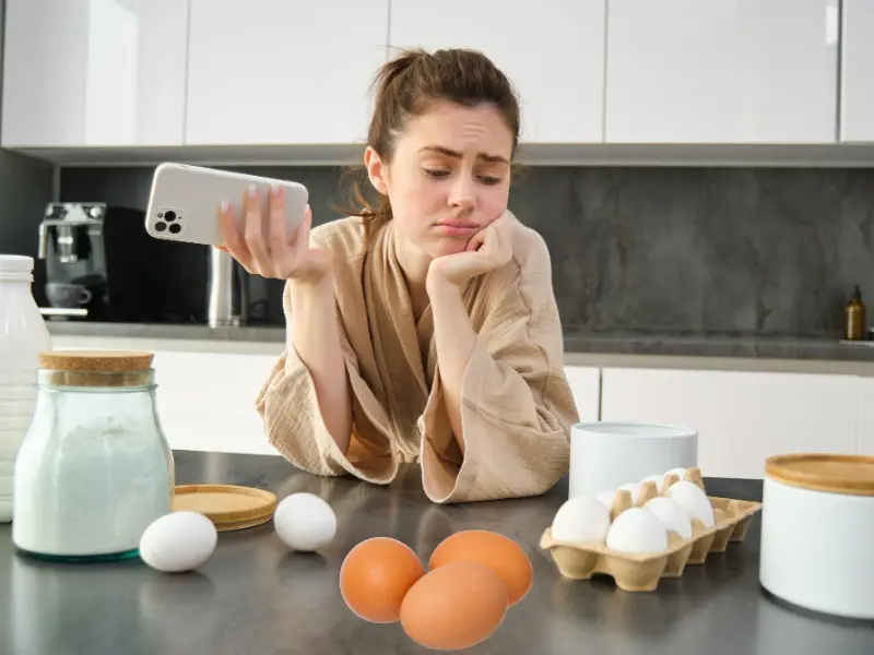 A young white girl, holding iphone, looking sad and observing the eggs placed in the kichen